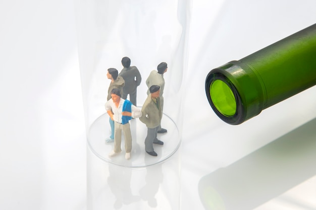 Miniature people. man addicted to alcohol on the background of a bottle of wine and a glass. the problem of alcoholism in society and family relations.