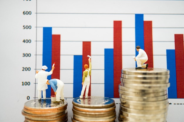 Miniature people, man painting bar graph on stack of coins 