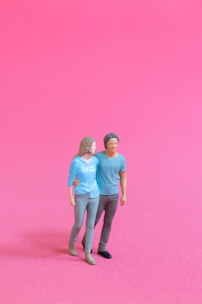 Miniature people man and woman in casual cloth standing together on pink background