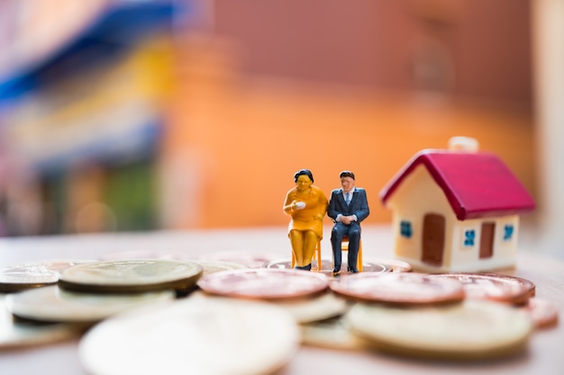 Miniature people, man and woman sitting on stack coins