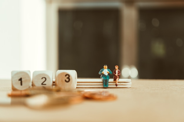 Miniature people, man and woman sitting with wooden number block and stack coins using as business a