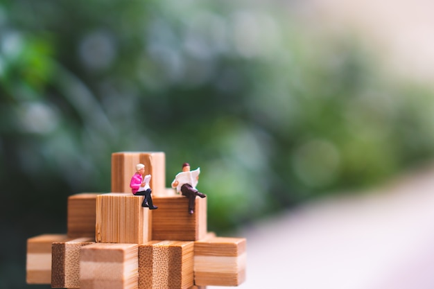 Miniature people, man and woman sitting on wooden interlocking 