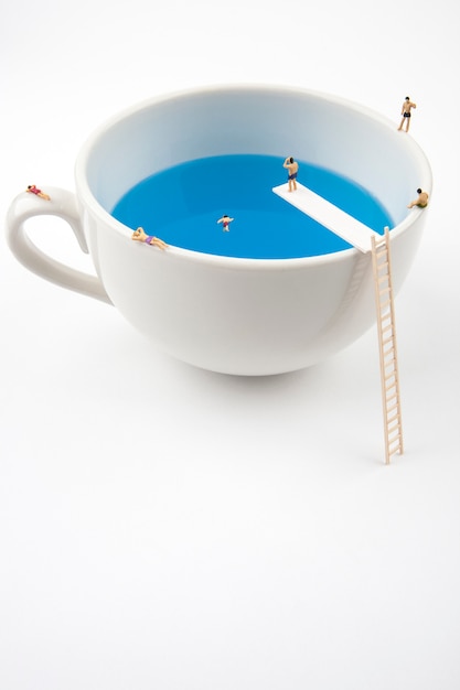 Miniature people in mug cup swimming pool