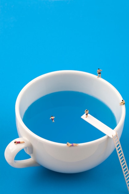 Miniature people in mug cup swimming pool