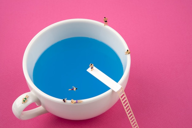 Miniature people in mug cup swimming pool