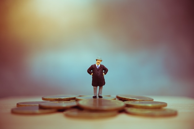 Miniature people, old businessman standing on stack coin using as business and financial concept - V