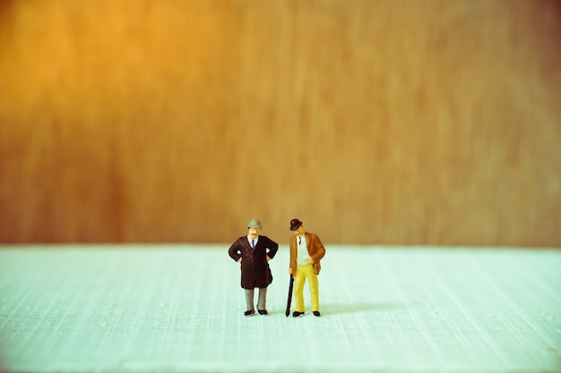 Miniature people, old couple businessman standing on wooden background using for business and teamwo