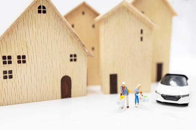 Foto persone in miniatura: genitore e figli con il carrello in piedi sulla pila di monete con casa e auto. concetto di shopping in abitazioni e veicoli.