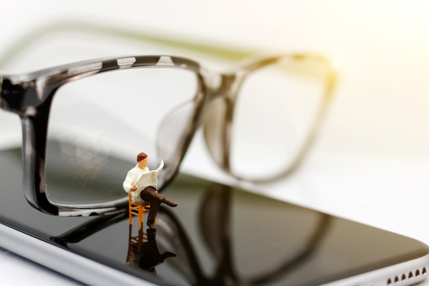 Miniature people reading newpapers with glasses.