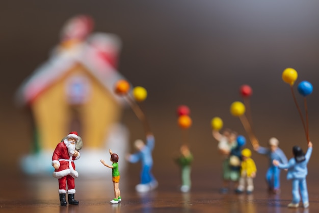 Миниатюрные люди: Санта-Клаус и дети, держащие воздушный шар