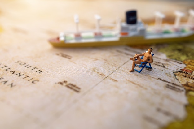 La gente miniatura si siede sui sedili prendisole della spiaggia sulla mappa di mondo d'annata e sulla nave, sul viaggio e sul concetto dell'estate.