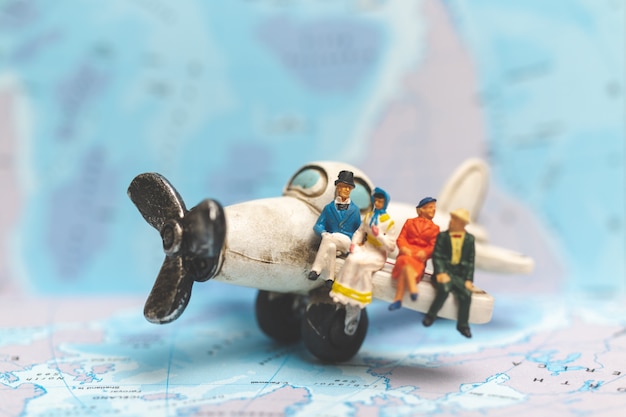 Miniature people sitting on The Airplane with world map background