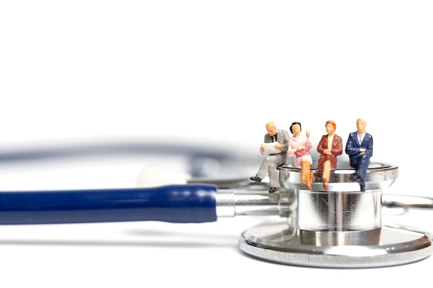 Miniature people sitting on a stethoscope on white background 