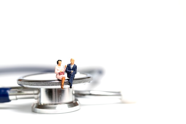 Miniature people sitting on a stethoscope on white background 