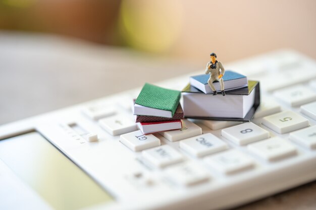 Miniature people sitting on white calculator using as background business 