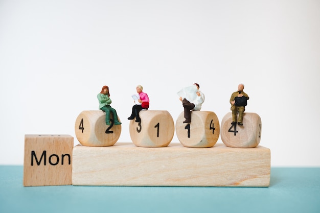 Miniature people sitting on wooden block number