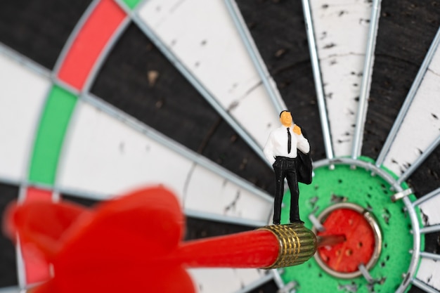 Photo miniature people: small business man on red dart arrow hitting in the target center of dartboard.