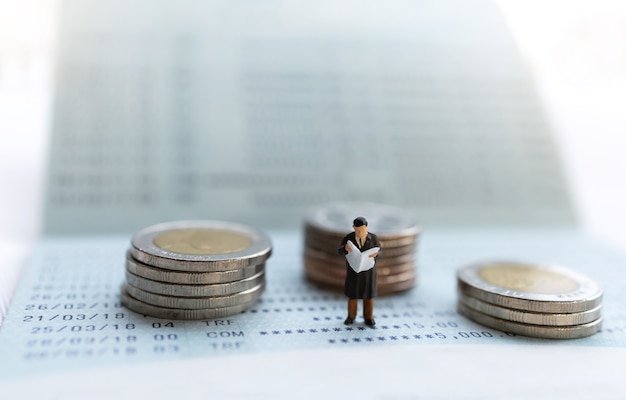 Miniature people stand on the bank passbook and coins stack, retirement concepts