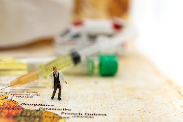 Photo miniature people stand on world map with ambulance car, medical mask and syringe of covid-19 vaccine . vaccine and healthcare medical concept.