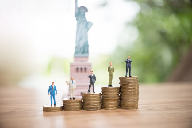 Miniature people standing on coin with statue of liberty