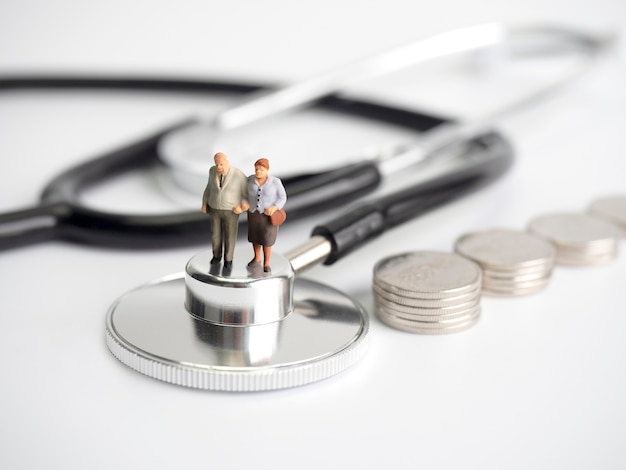 Miniature people standing on medical stethoscope with coins stack.