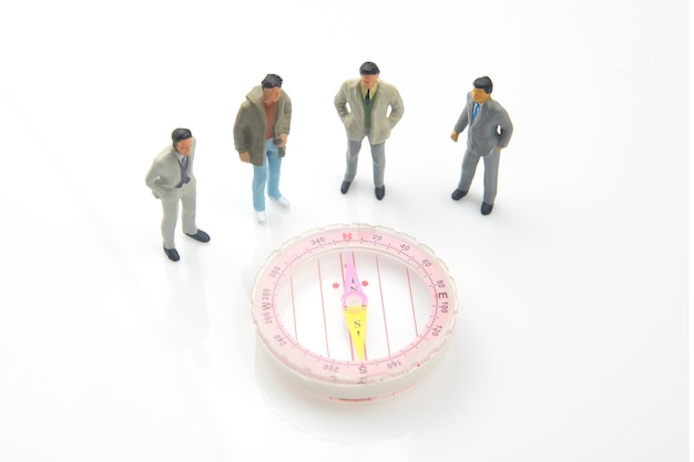 Miniature people standing near a compass on white background