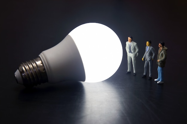 Miniature people standing near a Led lightbulb