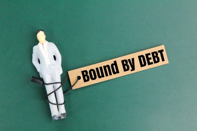 사진 빚에 묶여 있다는 단어로 둘러싸인 미니어처 사람들은 빚을 지거나 빚에 묶여 있다는 개념입니다.