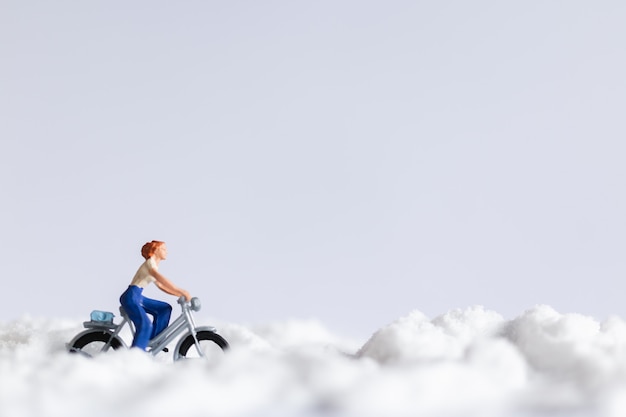 Persone in miniatura: viaggiatori che vanno in bicicletta sulla neve