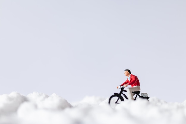 Persone in miniatura: viaggiatori che vanno in bicicletta sulla neve