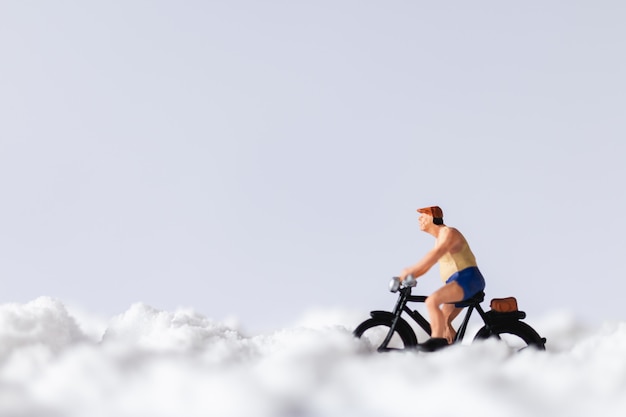 Persone in miniatura: viaggiatori che vanno in bicicletta sulla neve