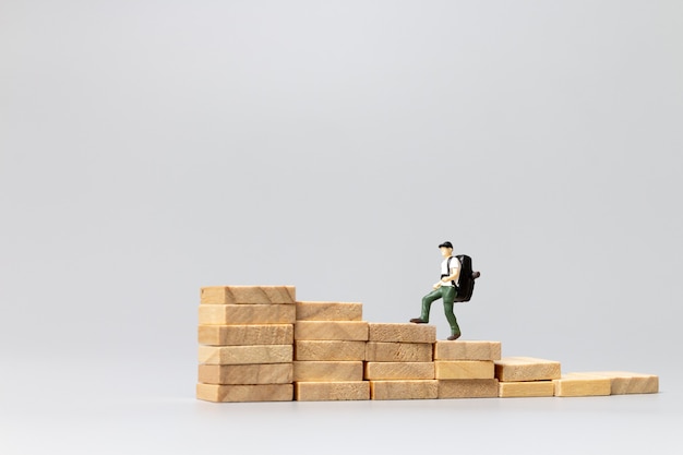 Миниатюрный путешественник людей, стоящий на деревянном блоке на сером фоне. Концепция путешествий и приключений