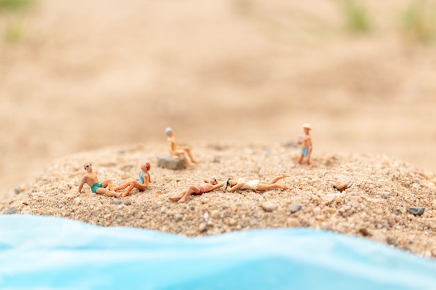 Miniature people wearing swimsuit relaxing on the beach