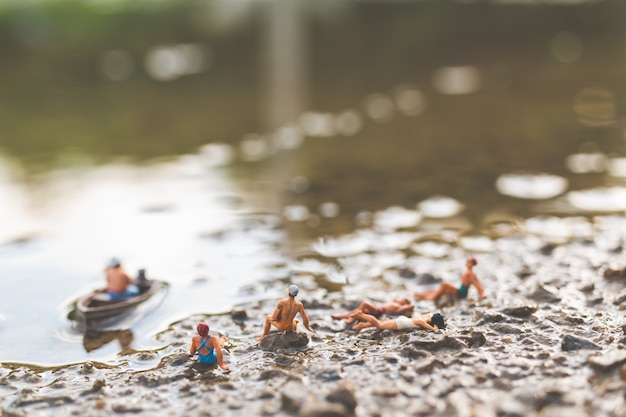 Miniature people wearing swimsuit relaxing on the beach