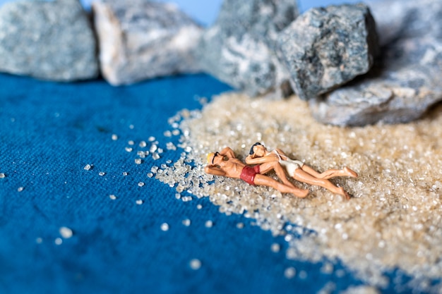 Miniature people wearing swimsuit relaxing on the beach