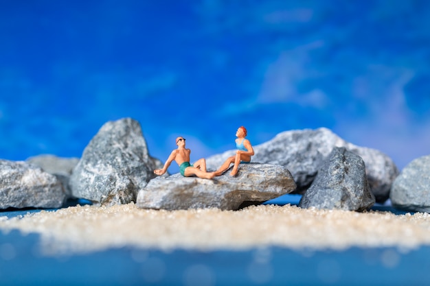 Miniature people wearing swimsuit relaxing on the beach