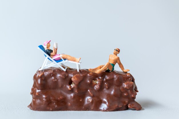 Miniature people wearing swimsuit relaxing on chocolate bars on gray background World Chocolate Day Concept