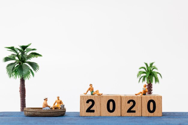 Miniature people wearing swimsuit relaxing  sitting on wooden block number 2020 