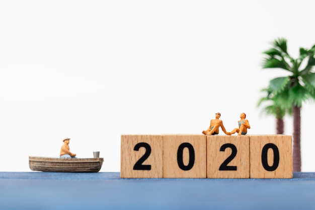 Miniature people wearing swimsuit relaxing  sitting on wooden block number 2020 