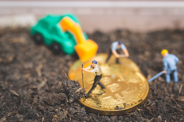 Miniature people: Worker team digging ground to uncover big shiny bitcoin 