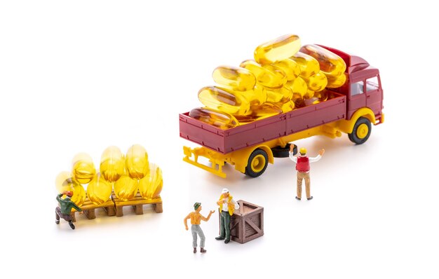 Miniature people workers transportation fish oil supplement capsules by truck isolated on white background, health care and medical business concept.