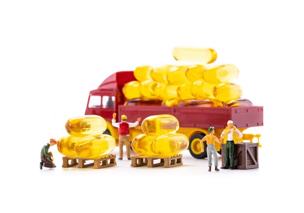 Miniature people workers transportation fish oil supplement capsules by truck isolated on white background, health care and medical business concept.