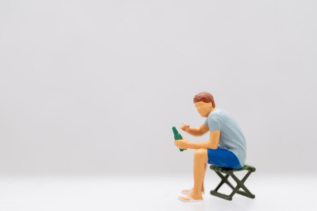 Foto persone in miniatura giovane seduto su una sedia da prato mentre afferra una bottiglia d'acqua