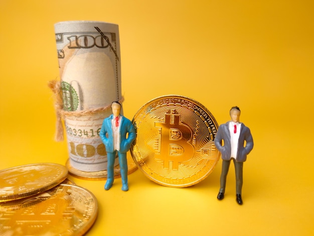 Miniature peoplebanknotes and bitcoins on a yellow backgroundDigital currency and business concept