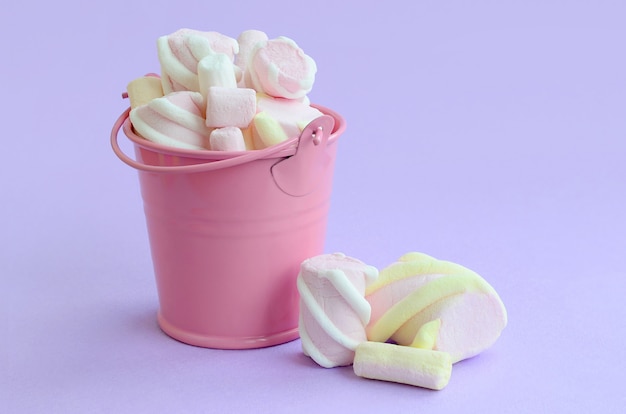 A miniature pink bucket filled with marshmallow lies on a violet pastel background