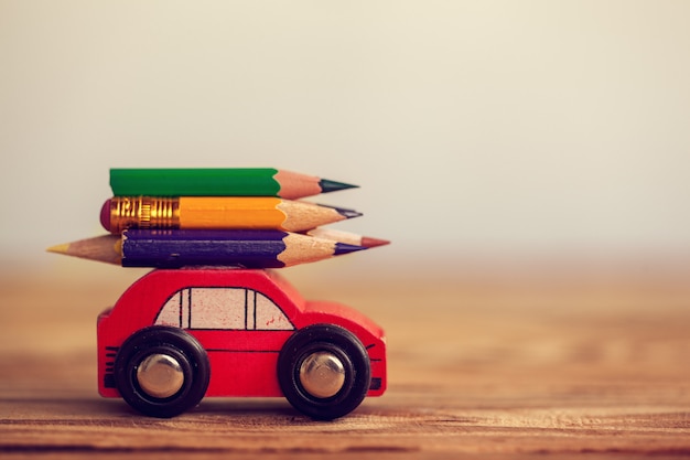 木製のテーブルの上にカラフルな鉛筆を運ぶミニチュアの赤い車。学校のコンセプトに戻る