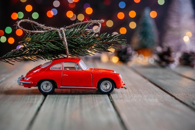 Auto rossa in miniatura con abete su sfondo natalizio con luci di natale colorate bokeh