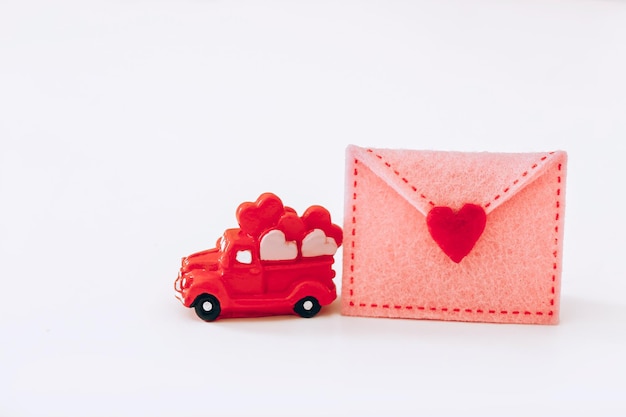Photo miniature red car with hearts and felt envelope on white background valentine day