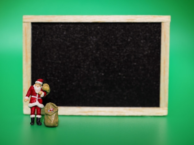 Miniature santa claus with blackboard on green background. Christmas and Happy New Year co