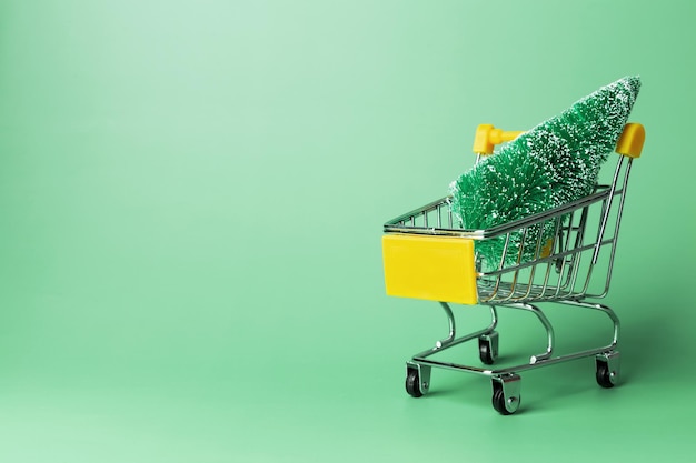 Miniature set model winter pine tree with snow in shopping cart on green background Soncept Christmas shopping holiday sales Copy space